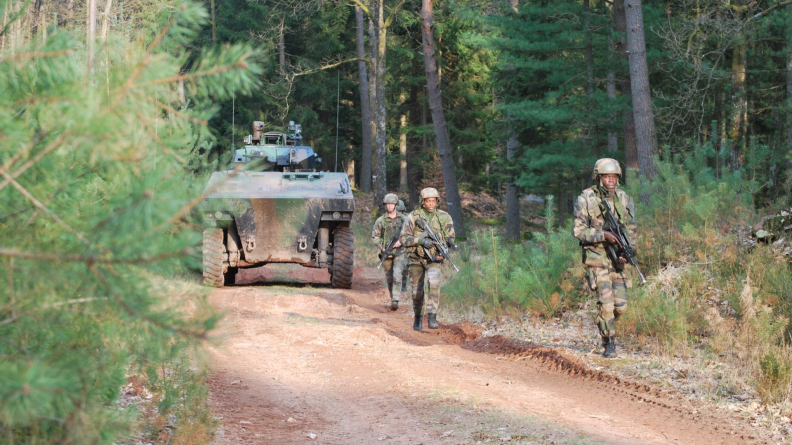 Trois soldats progressant le long d’un chemin forestier, suivis par un VBCI.