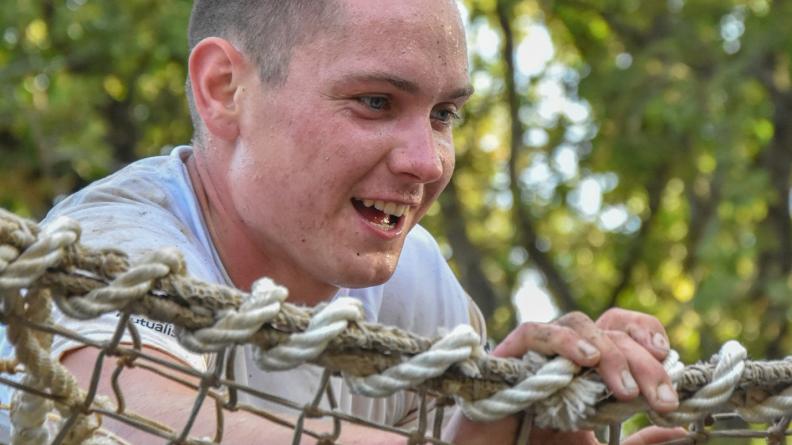 Participant arrivant au sommet du filet d’un obstacle du parcours à franchir