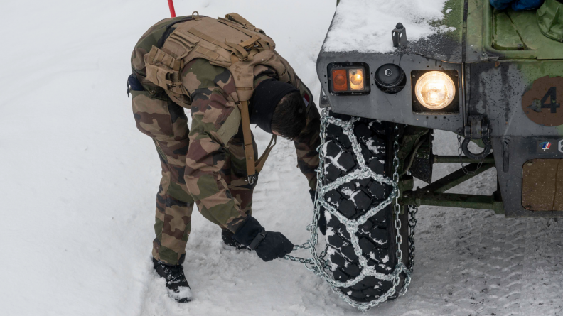 Un soldat français équipe les pneus de son véhicule de chaînes à neige.