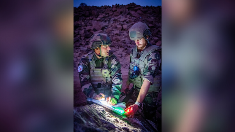 Deux soldats étudient la carte de nuit, à la lueur des lampes frontales.