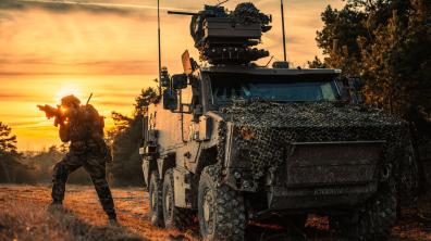 Entraînement tactique au crépuscule : coordination entre soldat et blindé en zone forestière.
